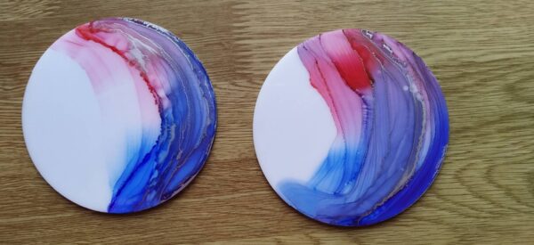 A picture of alcohol ink art coasters in round shape. There's a combination of red and blue with silver streaks across the surface of the coaster.